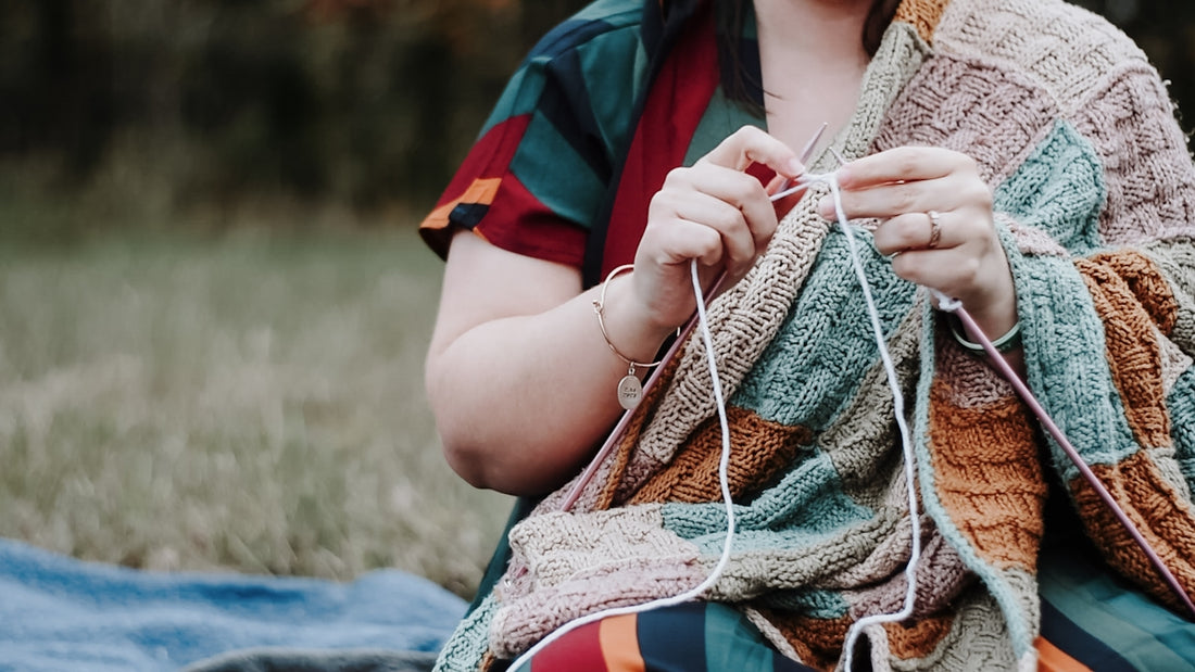 a woman sitting on the ground knitting a blanket