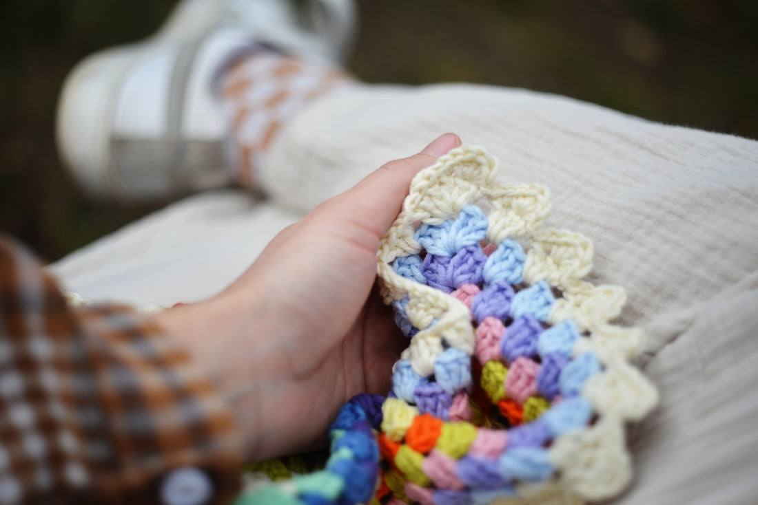 Person holding colorful crochet blanket with textured fabric.