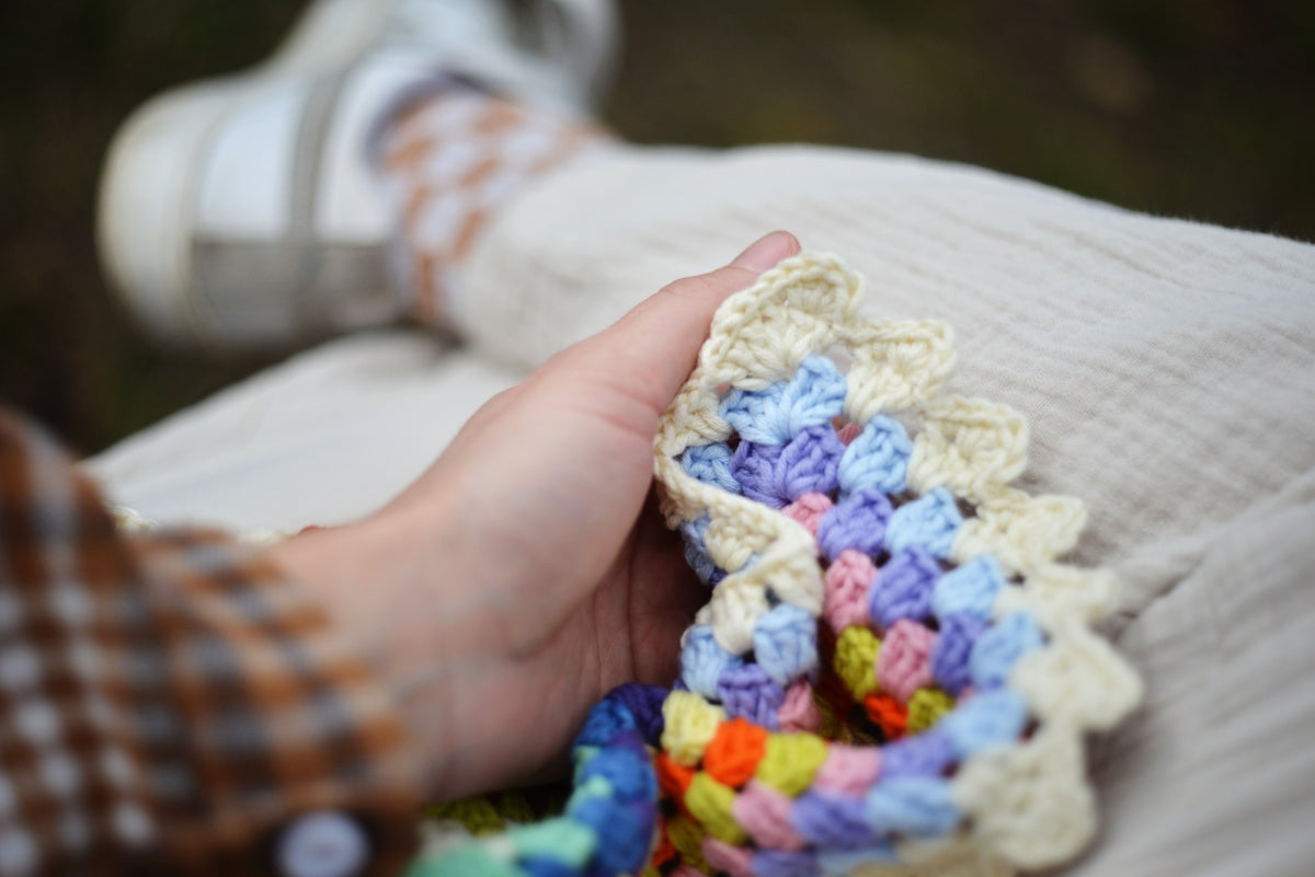 Person holding colorful crochet blanket with textured fabric.