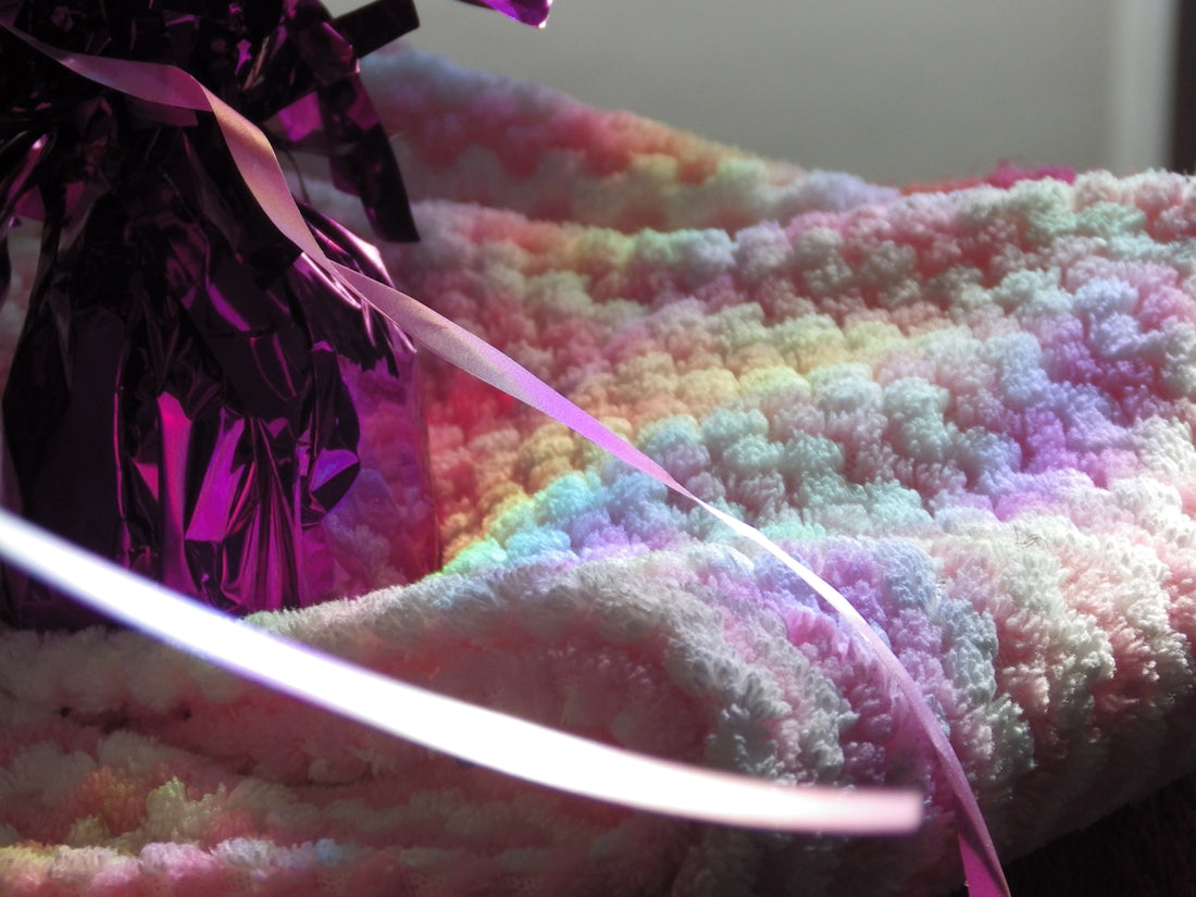A pastel crocheted blanket with a gift bag.