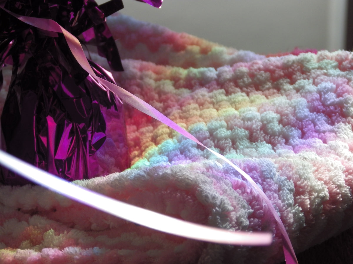 A pastel crocheted blanket with a gift bag.