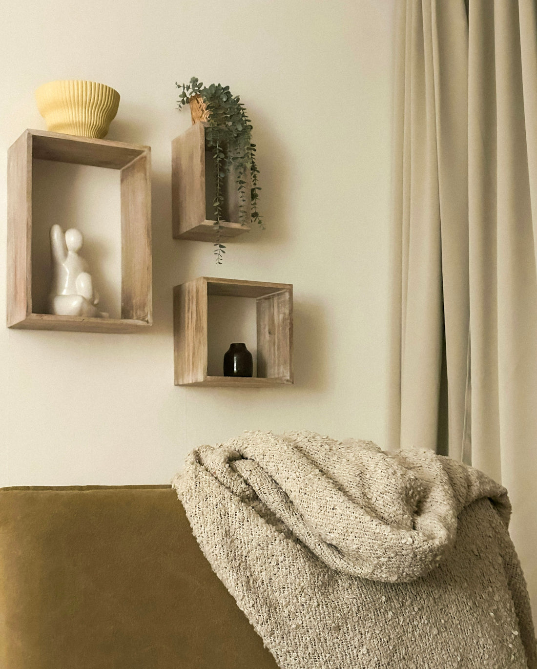 Three wooden shelves with decor above a couch and blanket.