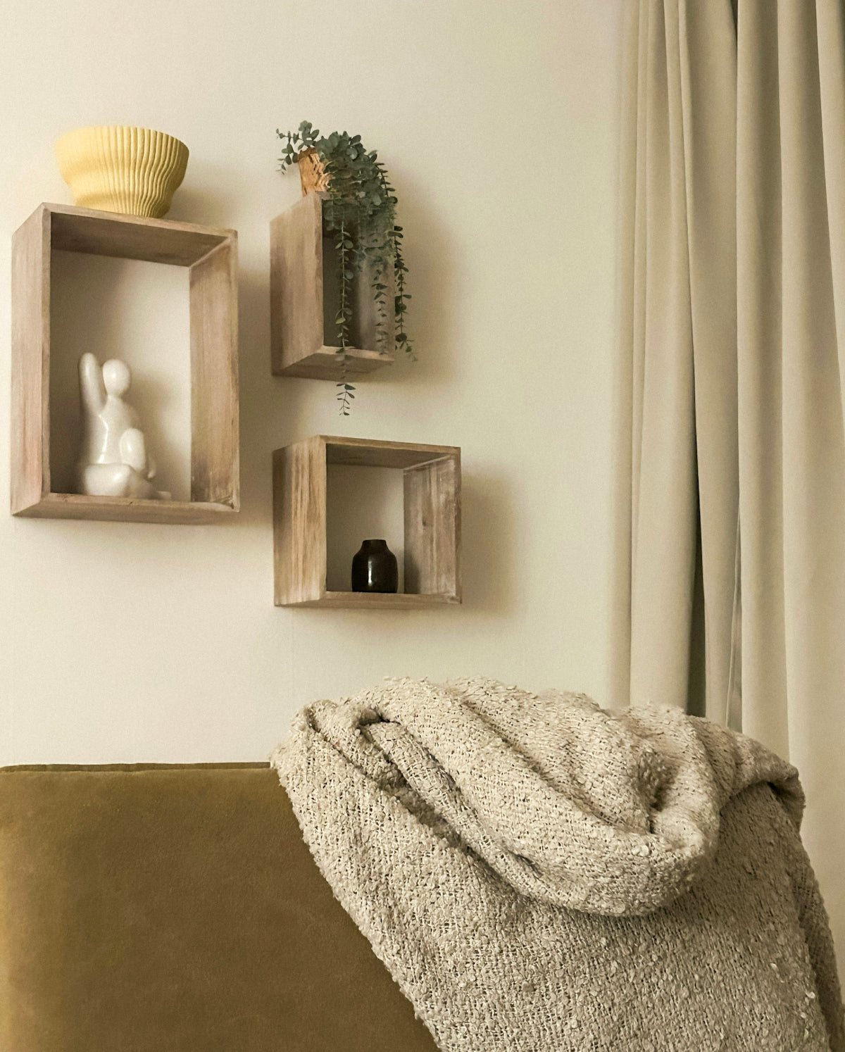 Three wooden shelves with decor above a couch and blanket.